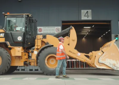 Een wiellader rijdt langs een lopende arbeider in een recyclingcentrum.