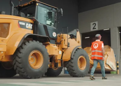 Een wiellader rijdt langs een lopende arbeider in een recyclingcentrum.