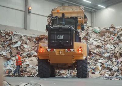 Een arbeider staat naast en kijkt omhoog naar een wiellader in een recyclingcentrum.