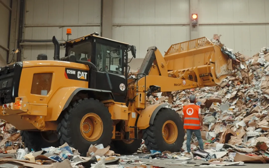 A worker standing alongside a wheel loader sorting garbage in a recycling center.