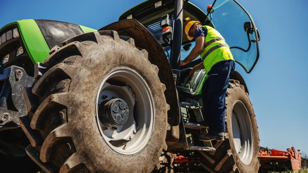 worker in hi-vis and hardhat on the stairs of a tractor with an open door
