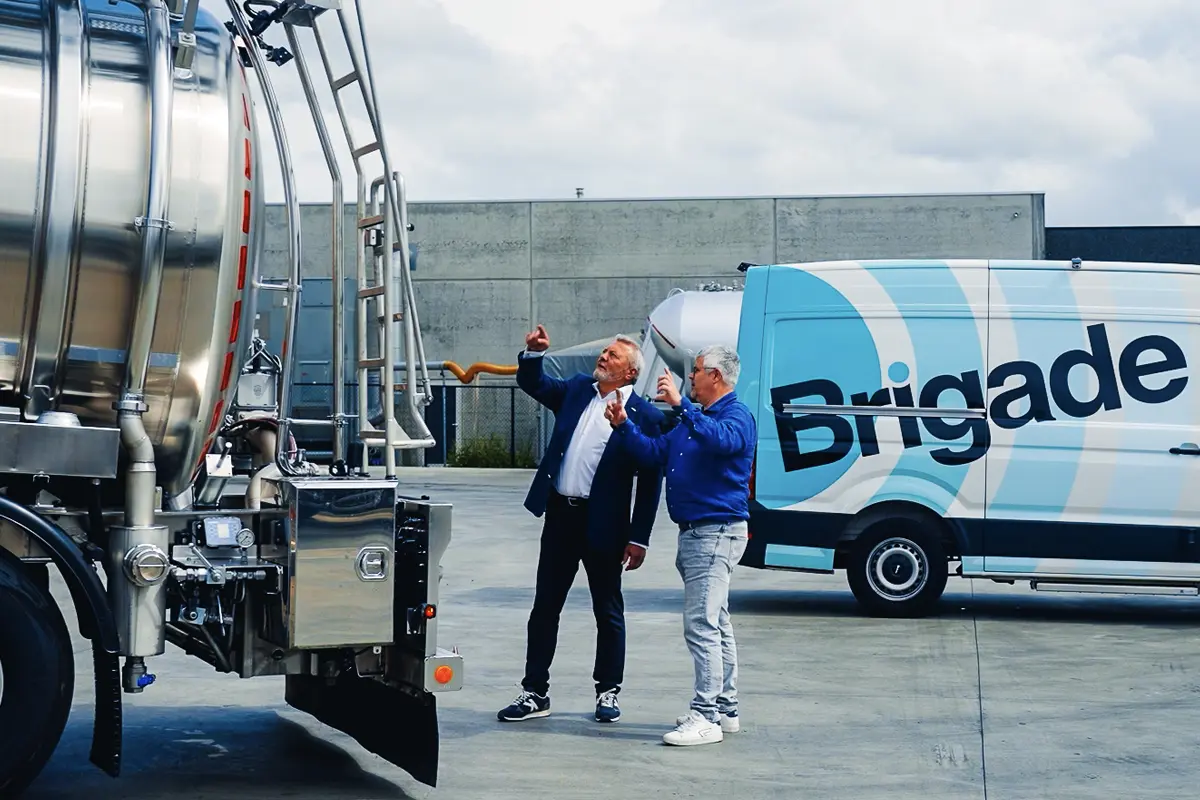 Un membre du personnel de Brigade et un employé de TVS Transport, debout à l'arrière d'un camion de TVS Transport, pointant du doigt la caméra d'intelligence artificielle