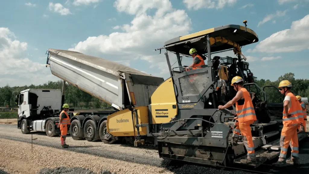 Budimex workers waiting for a road roller to finish being loaded with tar.